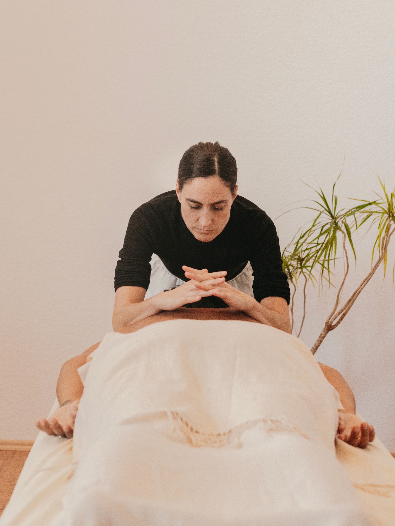 Sabina at the massage table, hands centered in a moment of stillness before a session