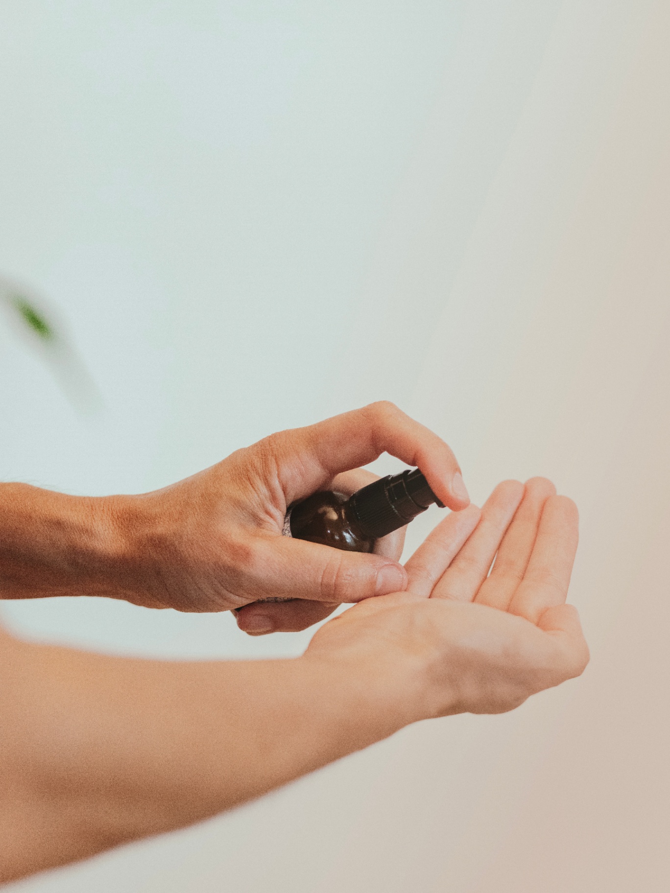 Hands dispensing a drop of facial serum from a small amber bottle